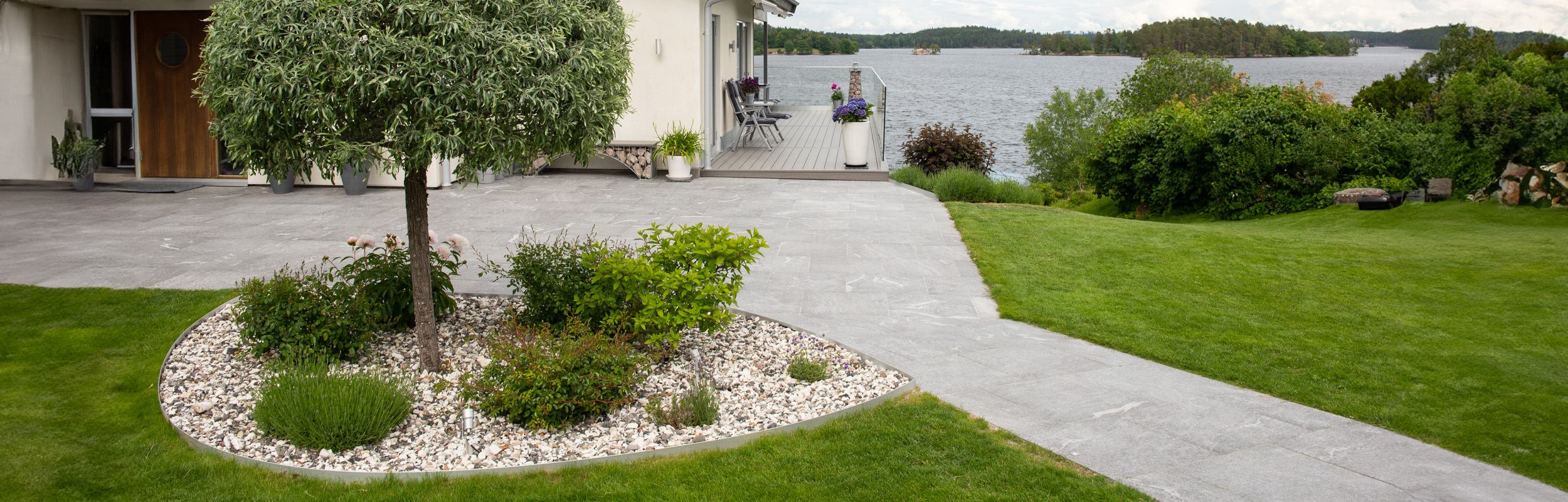 Stenbelagd yta med granitkeramik i grågrafit och stenrabatt med svartvit sjösten och kantstål i aluzink