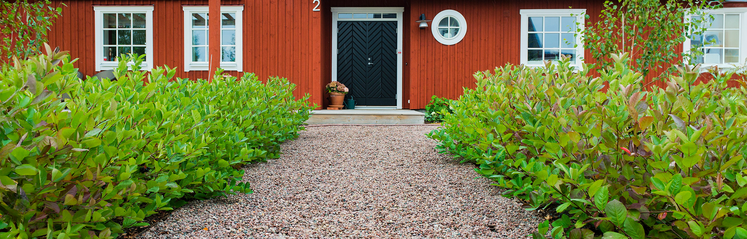 Naturröd gårdssingel i gång upp mot ett rött hus.